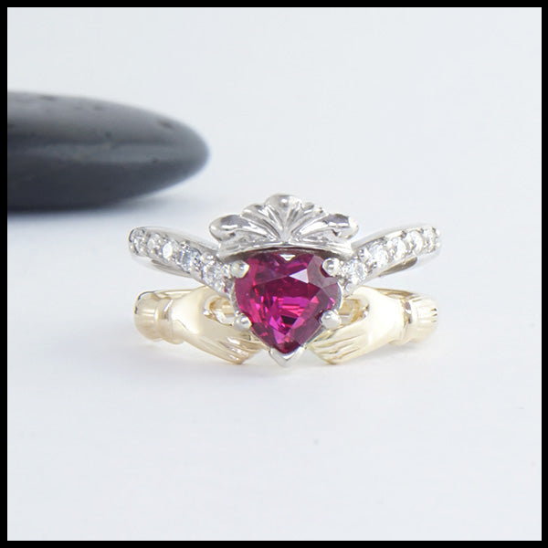 Two piece ring set in 14K White and Yellow Gold. One ring is set with a 1ct heart shaped Ruby and has 5 diamonds on either side. The other ring interlocks and holds the heart creating the traditional Claddagh.