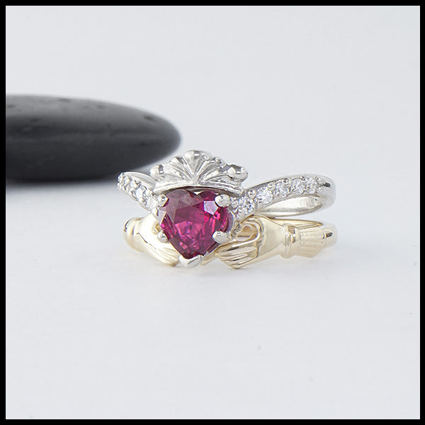 Two piece ring set in 14K White and Yellow Gold. One ring is set with a 1ct heart shaped Ruby and has 5 diamonds on either side. The other ring interlocks and holds the heart creating the traditional Claddagh.